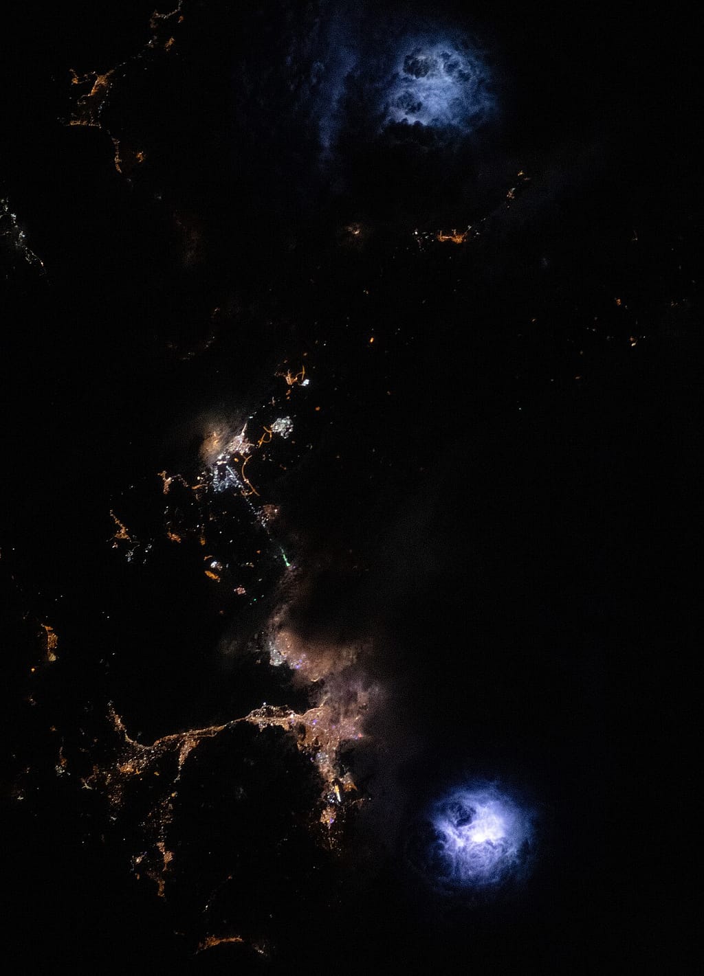 Thunderstorms glowing with lightning seen from above at night
