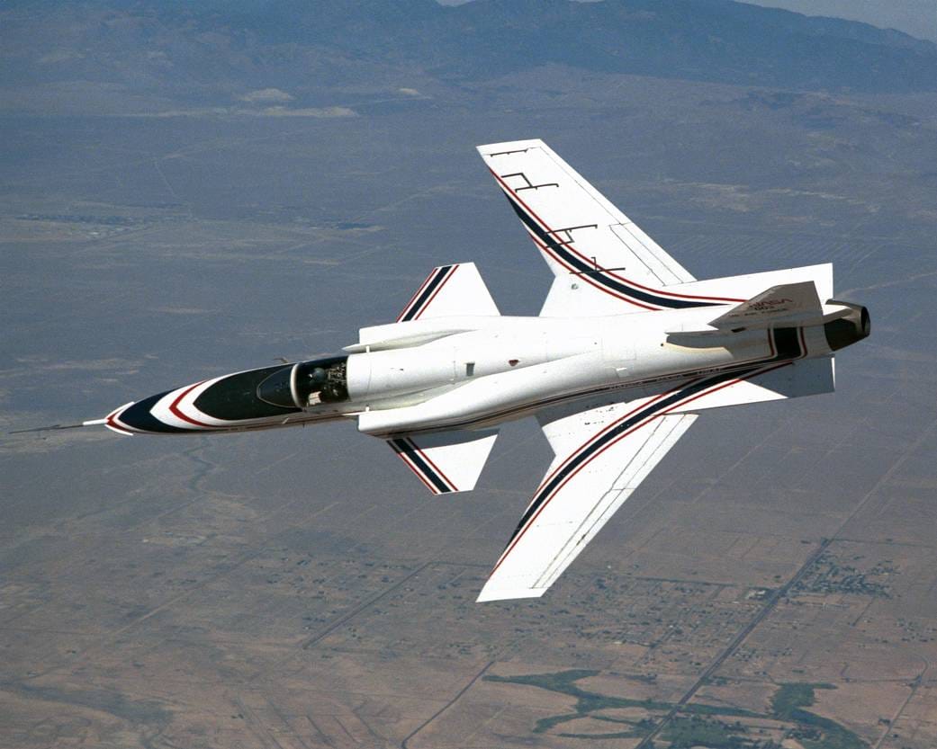 Un aereo Grumman X-29 ad ala a freccia inversa effettua una virata in volo sopra il deserto.