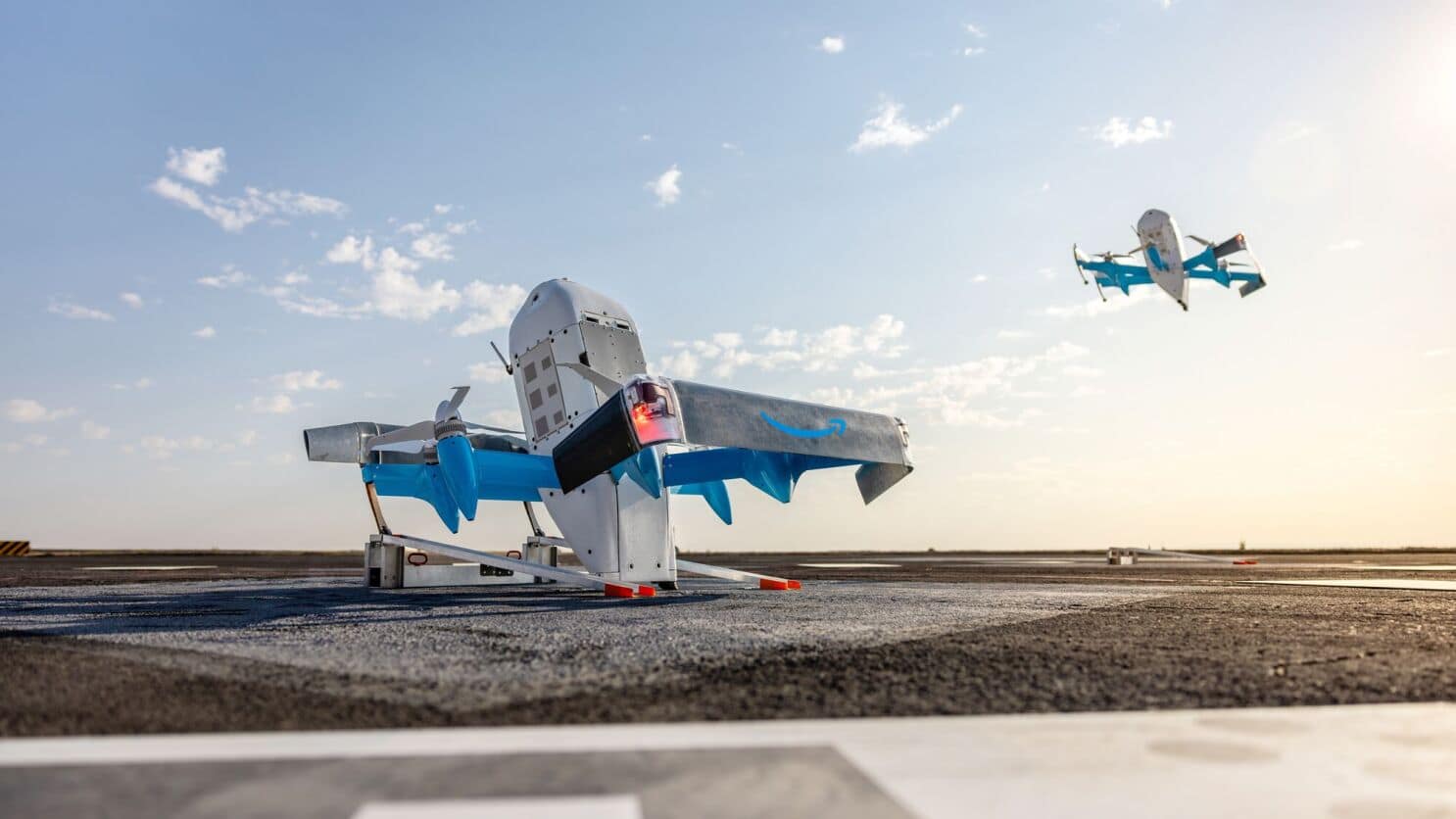 An Amazon Prime Air MK30 drone on its launch rail with another in flight