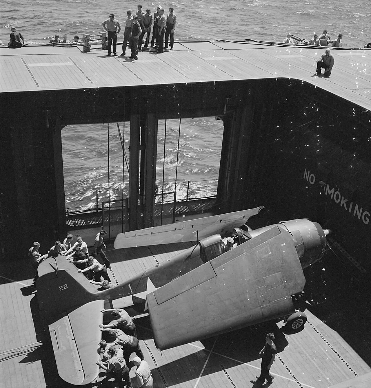 An F6F Hellcat pushed onto the flight deck elevator of USS Monterey, June 1944