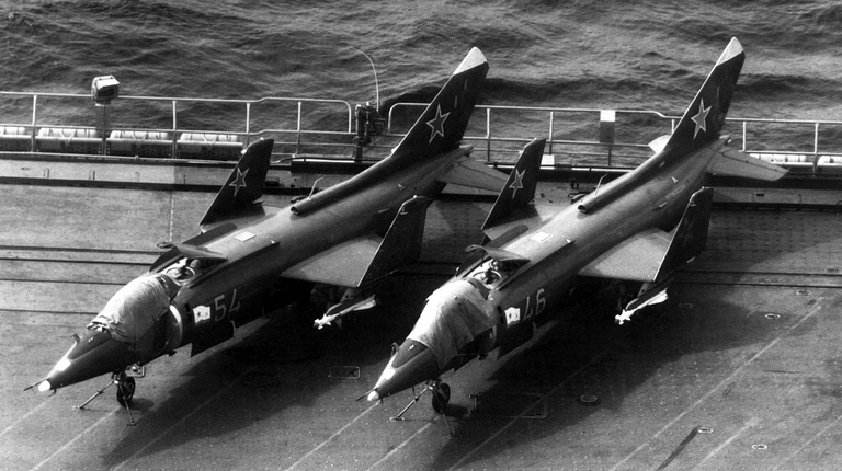 Two Yak-38s over a carrier deck, armed with AA-8 Aphid air-to-air missiles.