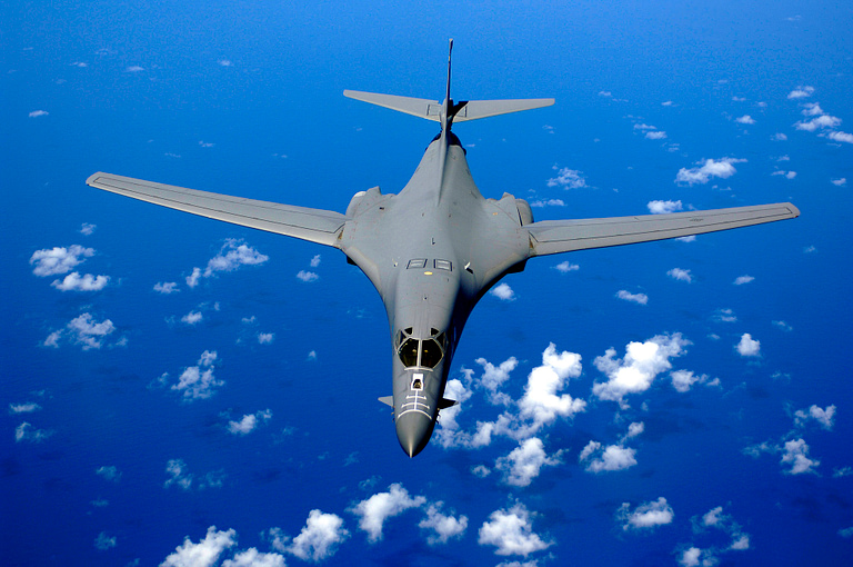 A B-1B Lancer over the Pacific wings swept for high-speed cruise.