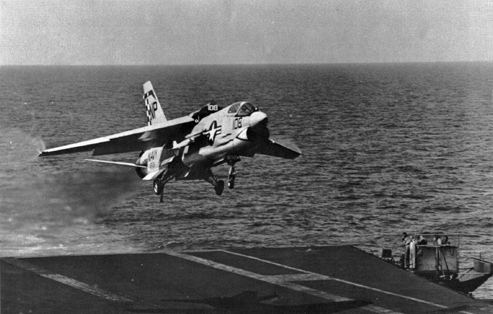 An F-8E of VF-211 on a carrier approach the variable-incidence wing raised for landing.