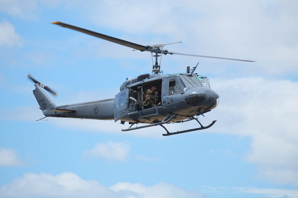 A UH-1H Iroquois in flight with its cabin doors slid wide open the classic Huey silhouette.