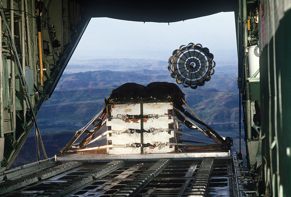 A heavy cargo pallet is airdropped from the rear ramp of a C-130 Hercules during a tactical airlift training flight.
