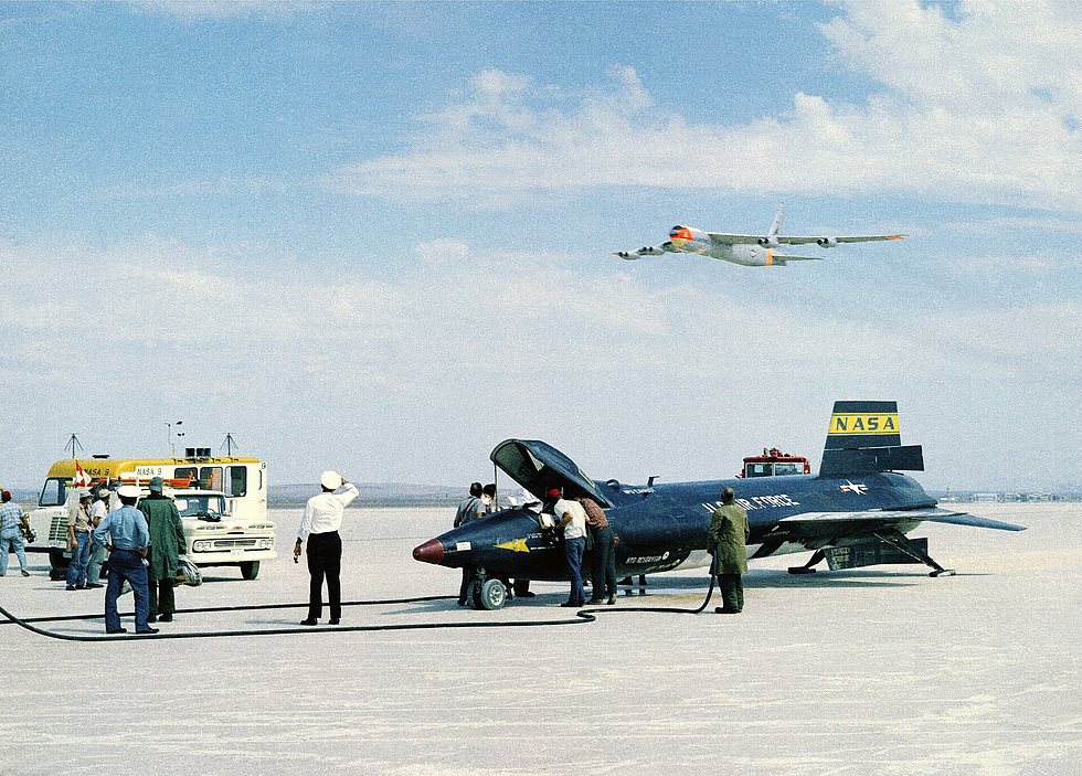 An X-15 on Rogers Dry Lake at Edwards after a dead-stick landing, the mothership overhead.